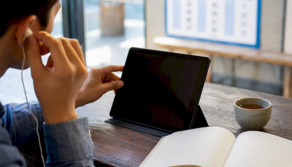 Hands adjusting earbuds near Mandarin study materials